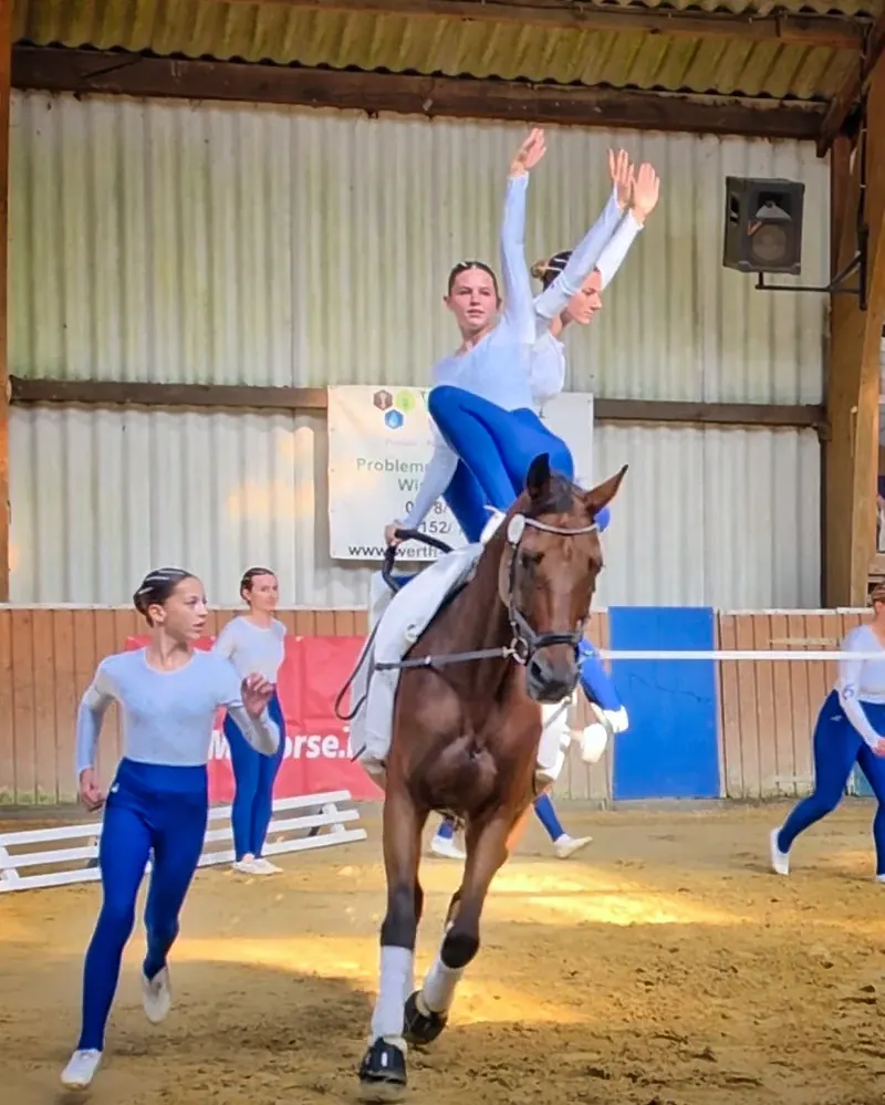 Training in der Reithalle: Zwei Voltigiererinnen turnen auf dem Pferd